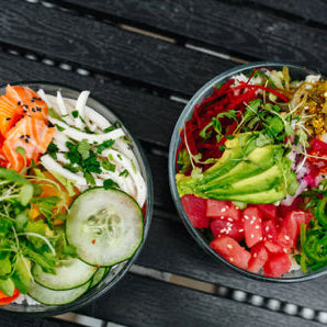 Two bowls of salad with various ingredients on a dark wooden surface